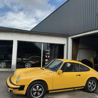 Un coupé ancien jaune devant l'atelier, carrosserie refaite.